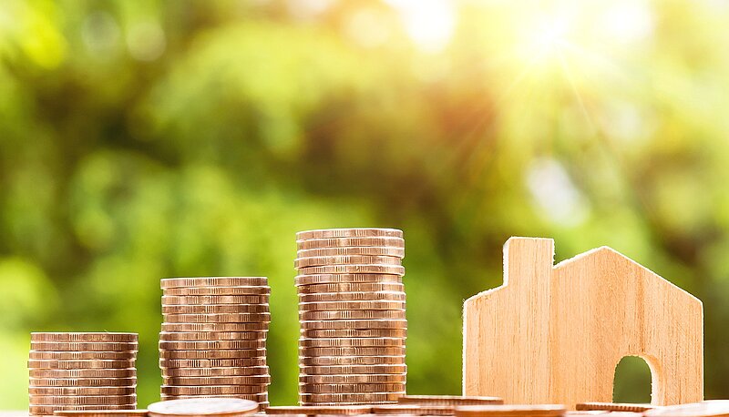 Drei höher werdende Stapel aus Geldmünzen und rechts daneben ein Holzhäuschen