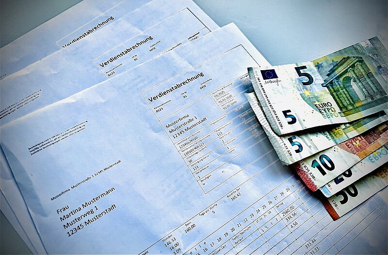 Muster einer Verdienstabrechnung mit daraufliegenden Geldscheinen