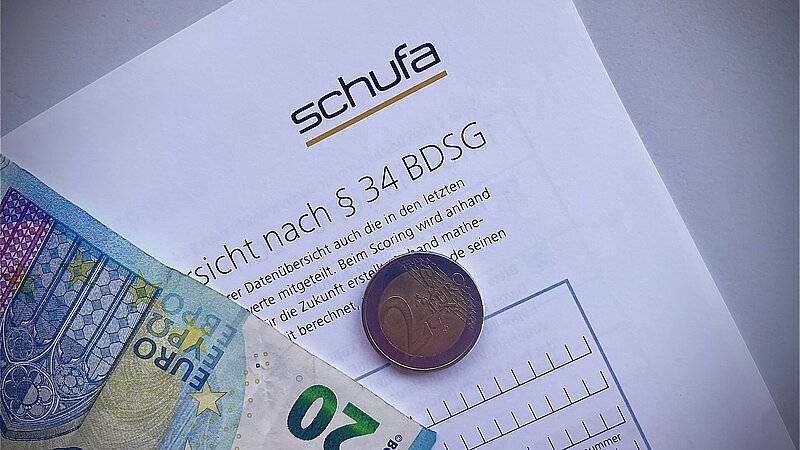 Ausschitt einer Schufa-Auskunft, darauf liegen eine 2 Euro Münze und ein 20 Euro Schein