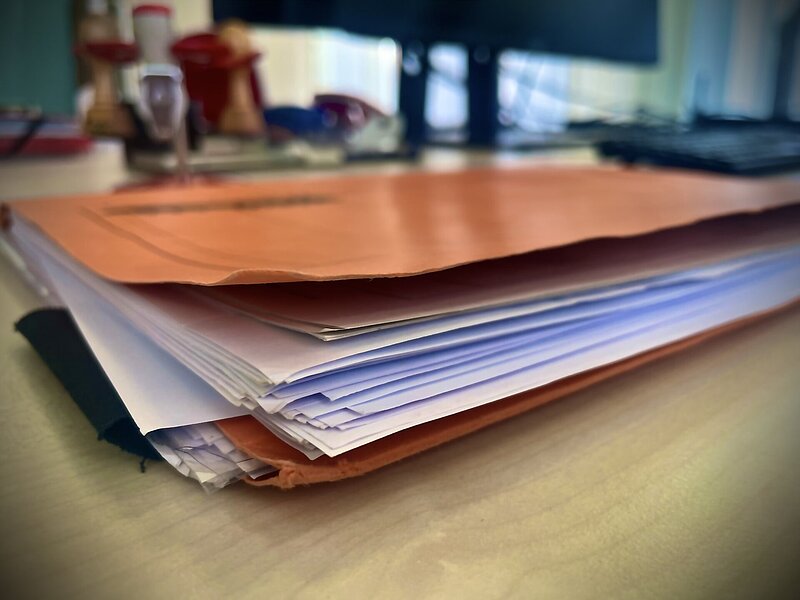 Auf einem Tisch liegt eine mit verschiedenen Dokumenten gefüllte braunrote Aktenmappe 